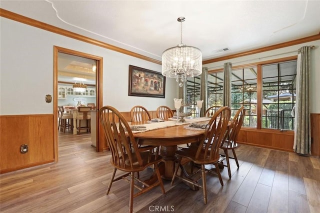 dining space featuring wood walls, crown molding, wood-type flooring, and an inviting chandelier