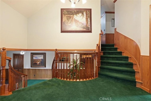 stairs with carpet floors, an inviting chandelier, vaulted ceiling, and wooden walls