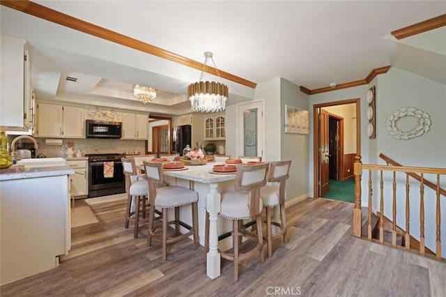 dining space with hardwood / wood-style flooring, a raised ceiling, sink, and a chandelier