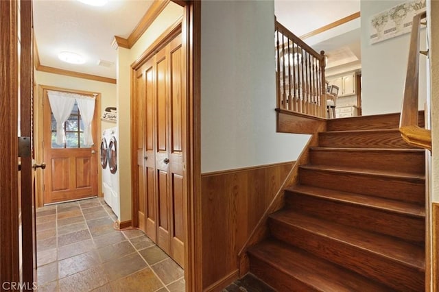 stairs with ornamental molding, washer and clothes dryer, and wooden walls