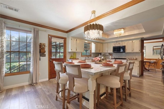 dining room with sink, a raised ceiling, a chandelier, light hardwood / wood-style floors, and ornamental molding