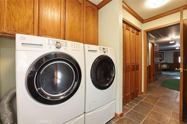 clothes washing area featuring washer and dryer, crown molding, and cabinets