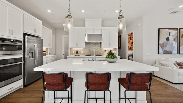 kitchen with backsplash, dark wood-type flooring, white cabinets, an island with sink, and stainless steel appliances