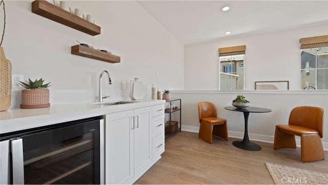 bar with lofted ceiling, sink, light hardwood / wood-style flooring, white cabinetry, and beverage cooler