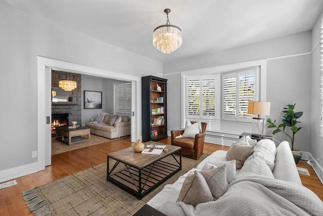 living room featuring a stone fireplace, hardwood / wood-style floors, and a chandelier