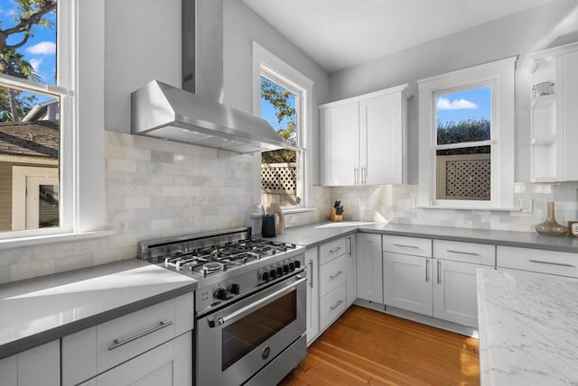 kitchen featuring wall chimney exhaust hood, white cabinetry, stainless steel stove, and decorative backsplash