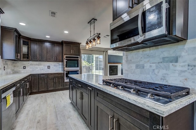 kitchen with hanging light fixtures, stainless steel appliances, tasteful backsplash, light hardwood / wood-style flooring, and dark brown cabinets