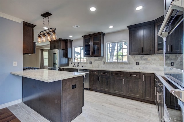 kitchen featuring appliances with stainless steel finishes, tasteful backsplash, crown molding, pendant lighting, and light hardwood / wood-style flooring