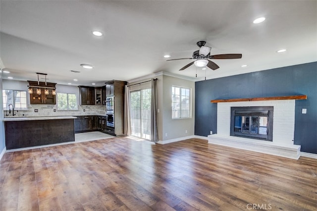 unfurnished living room featuring ceiling fan, sink, a brick fireplace, hardwood / wood-style flooring, and ornamental molding