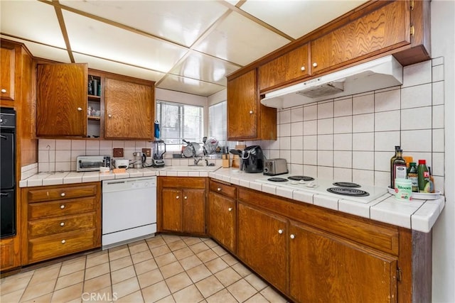 kitchen with under cabinet range hood, brown cabinets, white appliances, and tasteful backsplash