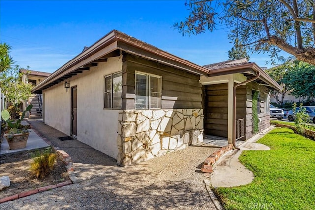 view of side of property with a yard, stone siding, and stucco siding