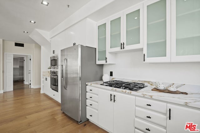 kitchen with white cabinets, stainless steel appliances, light stone counters, and light hardwood / wood-style floors