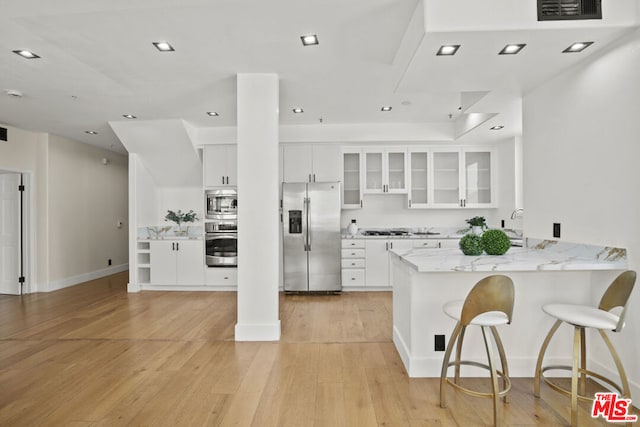 kitchen featuring kitchen peninsula, appliances with stainless steel finishes, a kitchen breakfast bar, light hardwood / wood-style flooring, and white cabinets