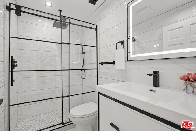 bathroom featuring vanity, toilet, a shower with door, and tile walls