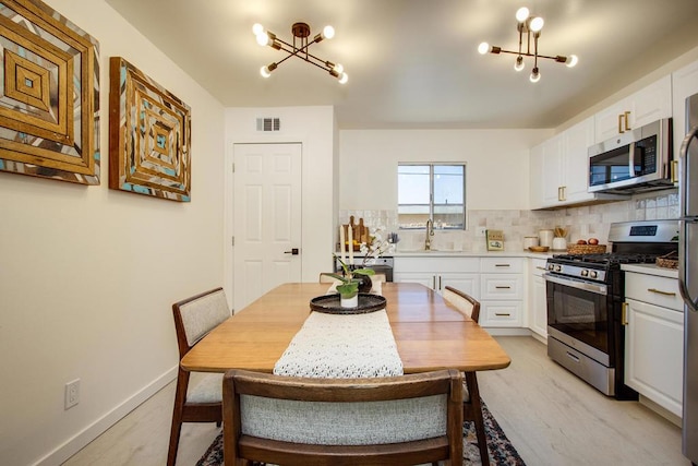 kitchen featuring sink, appliances with stainless steel finishes, tasteful backsplash, white cabinetry, and a chandelier