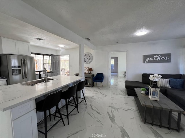 kitchen with stainless steel refrigerator with ice dispenser, a breakfast bar, a textured ceiling, sink, and white cabinetry