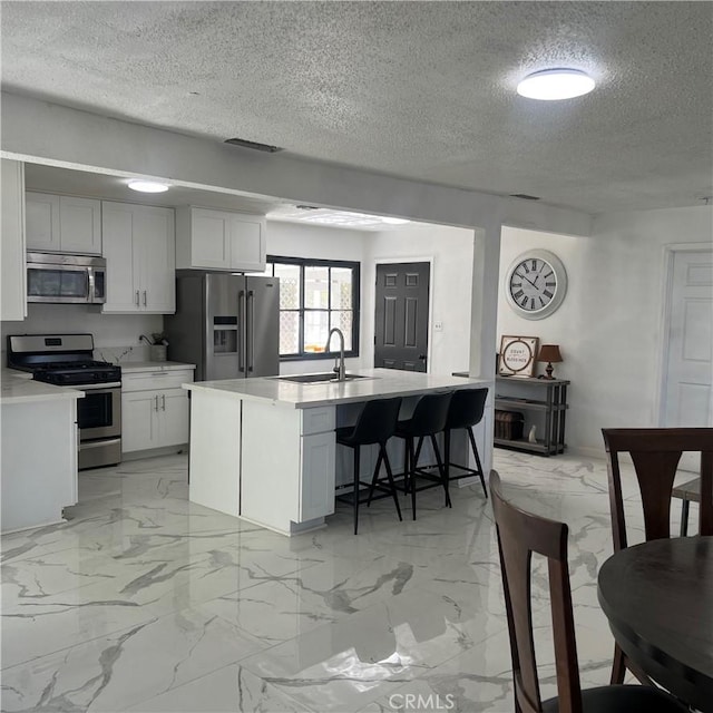 kitchen featuring a textured ceiling, white cabinets, stainless steel appliances, and a kitchen island with sink