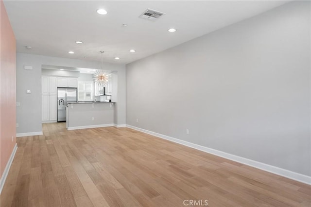 unfurnished living room with a notable chandelier and light hardwood / wood-style floors