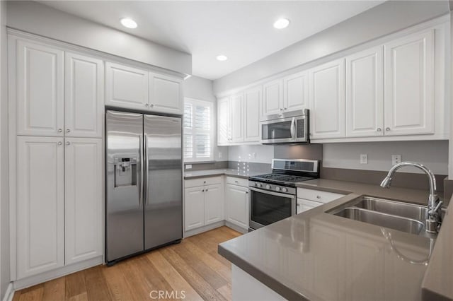 kitchen featuring light wood-type flooring, appliances with stainless steel finishes, white cabinets, and sink