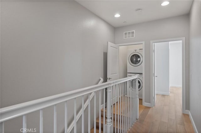 hall with stacked washer / drying machine and light wood-type flooring