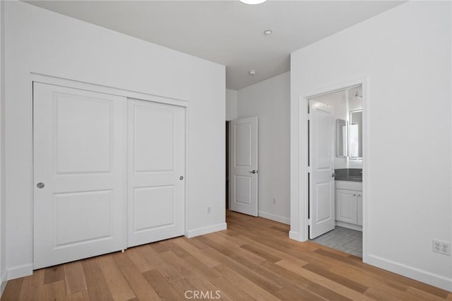 unfurnished bedroom with ensuite bathroom, a closet, and light hardwood / wood-style floors