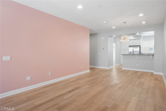 unfurnished living room with an inviting chandelier and light hardwood / wood-style floors