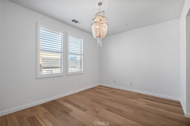 empty room featuring hardwood / wood-style flooring and a notable chandelier