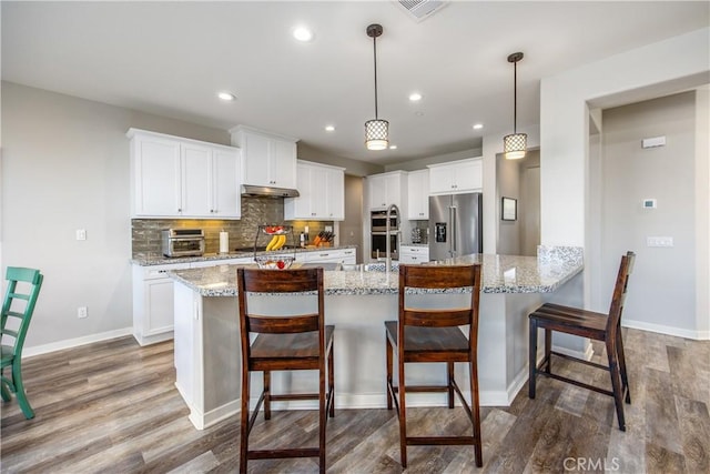 kitchen with white cabinets, appliances with stainless steel finishes, decorative light fixtures, and hardwood / wood-style flooring