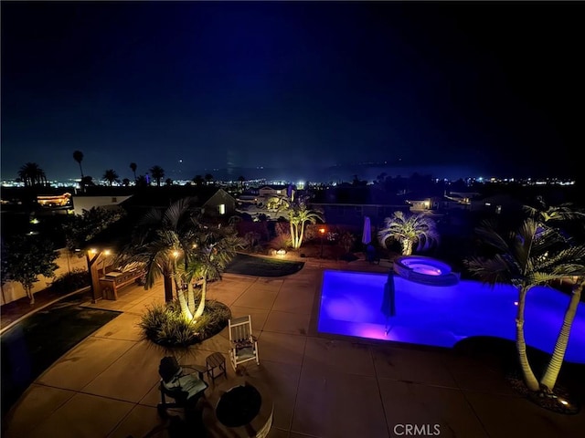 pool at night with a patio area and an in ground hot tub