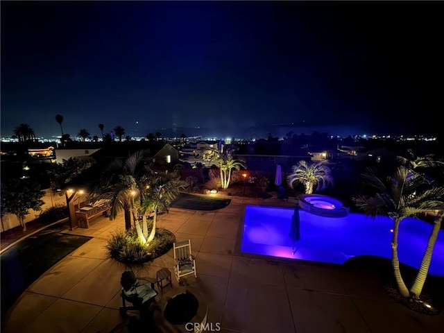 pool at twilight with a patio area and an in ground hot tub