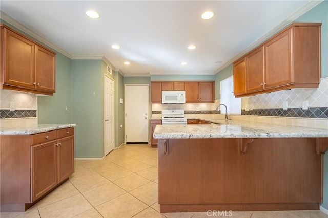 kitchen featuring kitchen peninsula, decorative backsplash, white appliances, sink, and a breakfast bar area