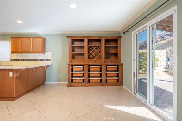 kitchen with light tile patterned floors, backsplash, light stone counters, and ornamental molding