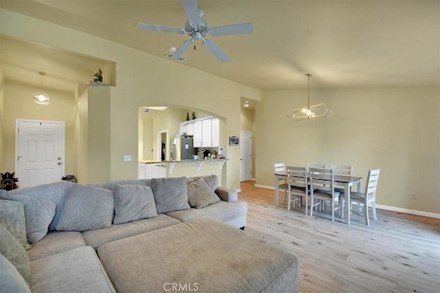 living room featuring ceiling fan with notable chandelier, light wood-type flooring, and lofted ceiling