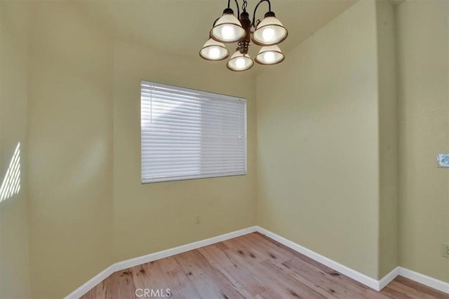 empty room featuring a notable chandelier and light wood-type flooring