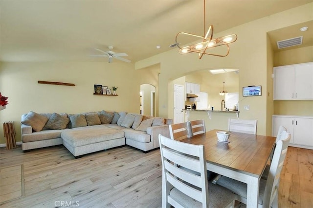 dining space featuring ceiling fan with notable chandelier, light wood-type flooring, and vaulted ceiling