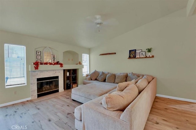 living room featuring ceiling fan, light hardwood / wood-style floors, lofted ceiling, and a tile fireplace