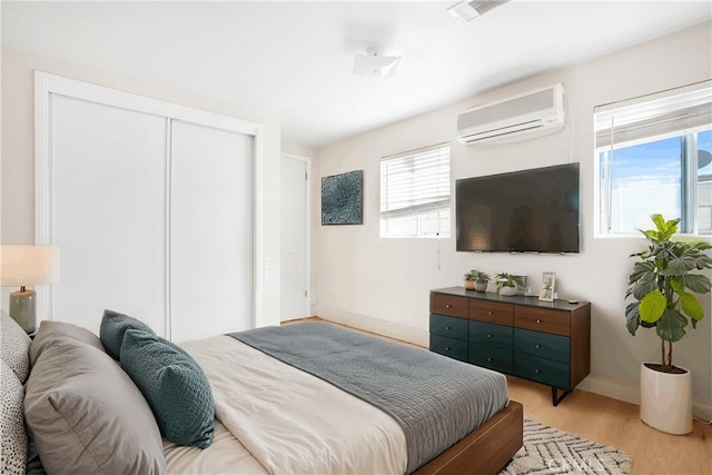 bedroom with a wall unit AC, multiple windows, and light hardwood / wood-style floors