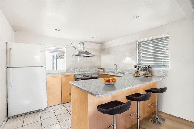 kitchen featuring a breakfast bar, sink, white fridge, kitchen peninsula, and extractor fan