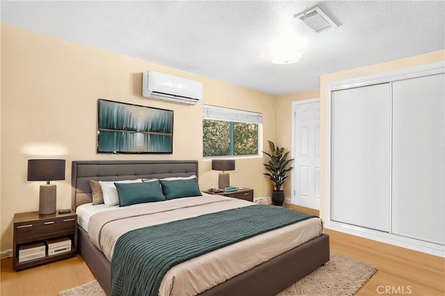 bedroom featuring a wall mounted AC, a closet, light hardwood / wood-style floors, and a textured ceiling