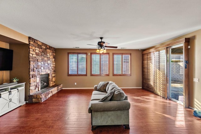 living room with a stone fireplace, ceiling fan, a textured ceiling, and hardwood / wood-style flooring