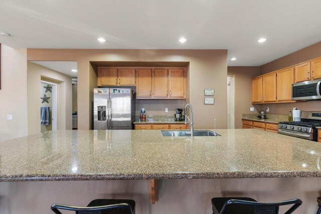 kitchen featuring a breakfast bar, a large island with sink, sink, appliances with stainless steel finishes, and light stone counters