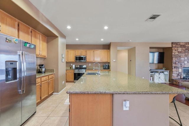 kitchen with light stone countertops, appliances with stainless steel finishes, a large island, and sink