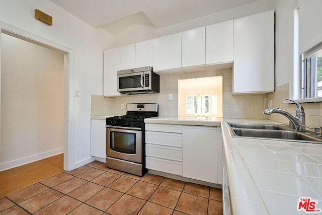 kitchen with white cabinetry, sink, stainless steel appliances, tasteful backsplash, and tile countertops