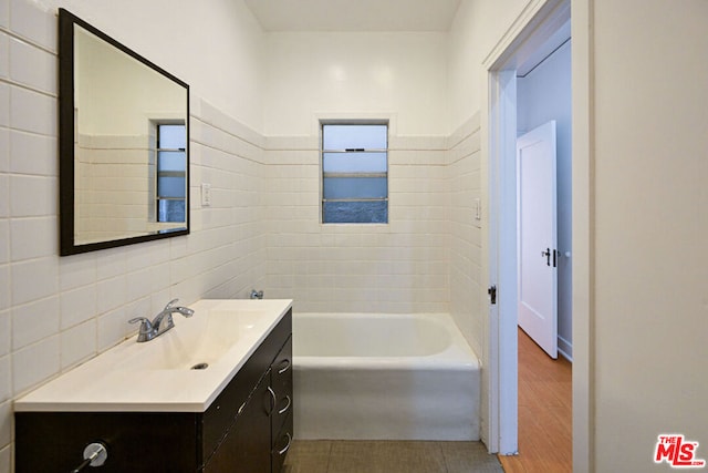 bathroom featuring hardwood / wood-style floors, vanity, tile walls, and a bathing tub