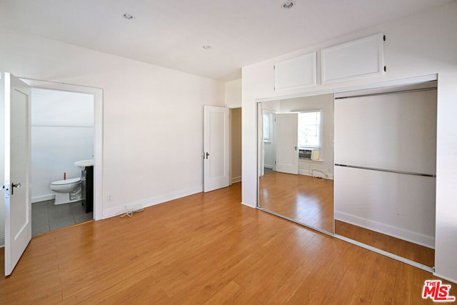 unfurnished bedroom featuring ensuite bath, light hardwood / wood-style flooring, a closet, and cooling unit