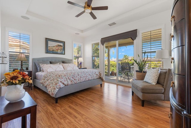 bedroom with ceiling fan, a raised ceiling, hardwood / wood-style floors, and access to outside