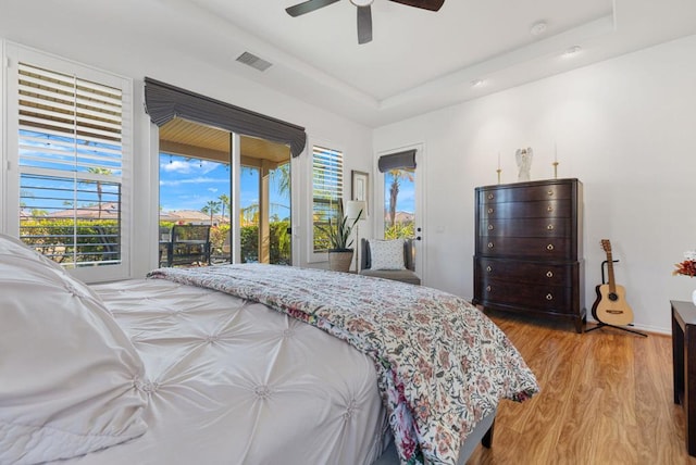 bedroom featuring access to exterior, a tray ceiling, light hardwood / wood-style flooring, and ceiling fan