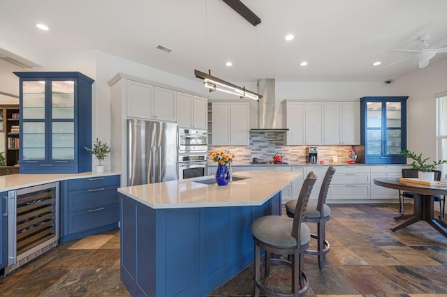 kitchen featuring wall chimney range hood, appliances with stainless steel finishes, white cabinetry, wine cooler, and decorative light fixtures