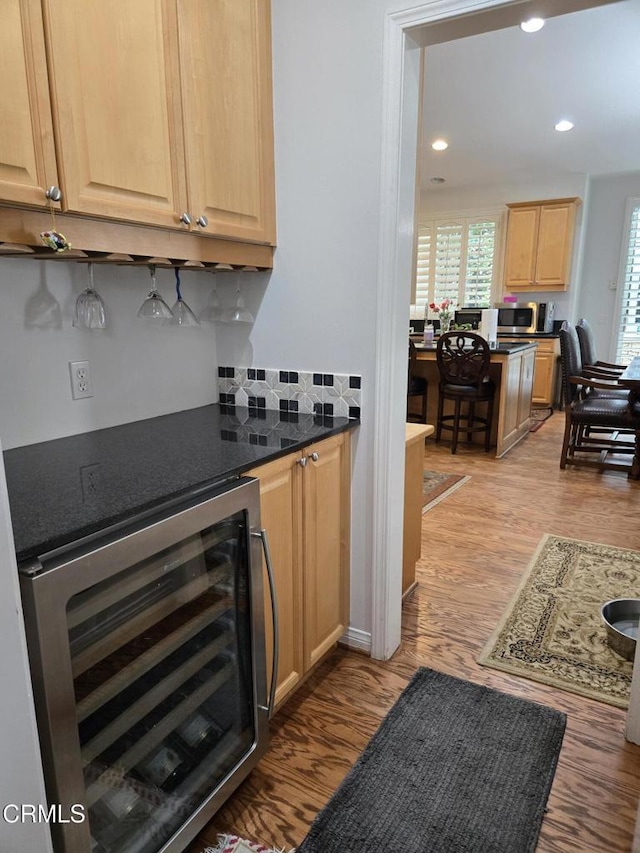 kitchen featuring light brown cabinets, dark stone countertops, light wood-type flooring, and beverage cooler