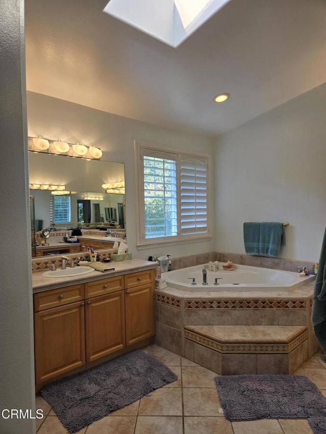 bathroom with tile patterned flooring, vanity, a relaxing tiled tub, and a skylight